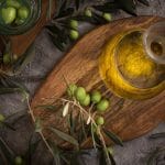 Extra virgin olive oil in glass bottle with branch of olives on rustic background low key