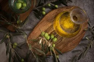 Extra virgin olive oil in glass bottle with branch of olives on rustic background low key