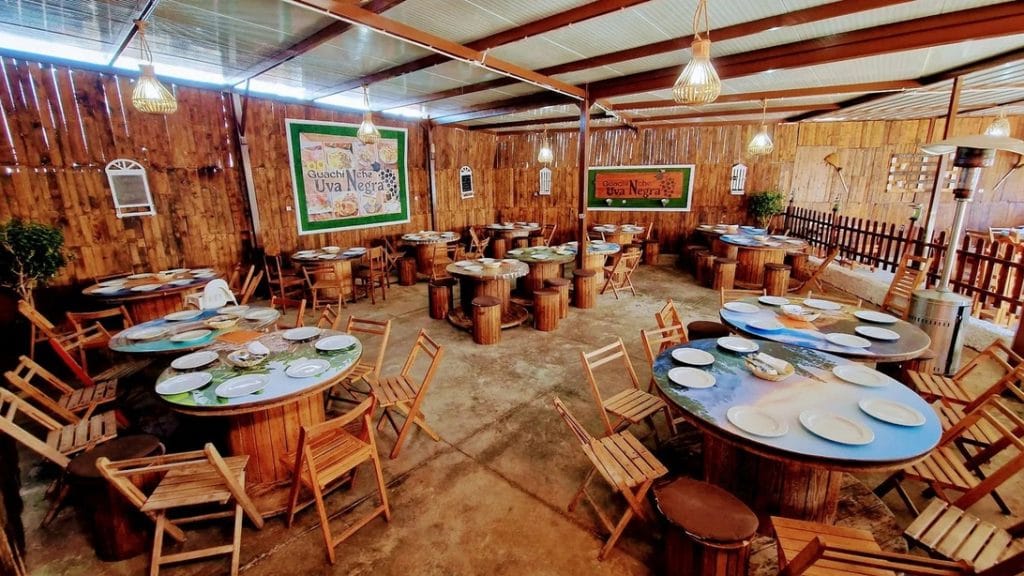 Rustic dining area with round barrel tables, wooden chairs, and warm hanging lights.