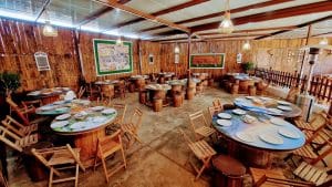 Rustic dining area with round barrel tables, wooden chairs, and warm hanging lights.