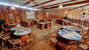 Rustic dining area with round barrel tables, wooden chairs, and warm hanging lights.