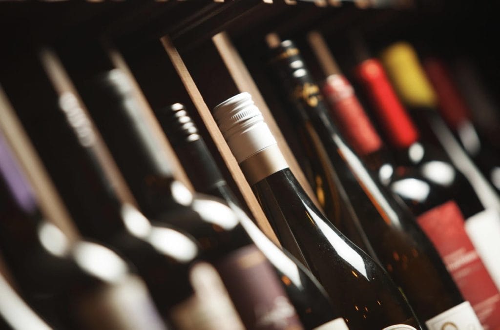 Wine bottles lined up on a shelf, foreground bottle with a white foil capsule in focus