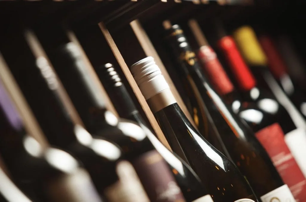 Wine bottles lined up on a shelf, foreground bottle with a white foil capsule in focus