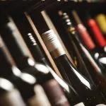 Wine bottles lined up on a shelf, foreground bottle with a white foil capsule in focus