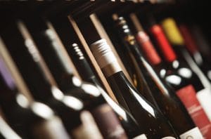 Wine bottles lined up on a shelf, foreground bottle with a white foil capsule in focus