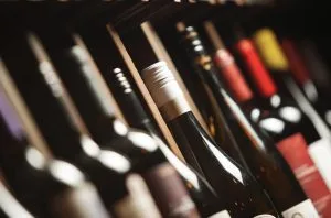 Wine bottles lined up on a shelf, foreground bottle with a white foil capsule in focus