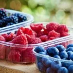 Assorted berries in clear plastic containers: raspberries, blueberries, and blackberries outdoors.