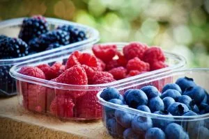 Assorted berries in clear plastic containers: raspberries, blueberries, and blackberries outdoors.